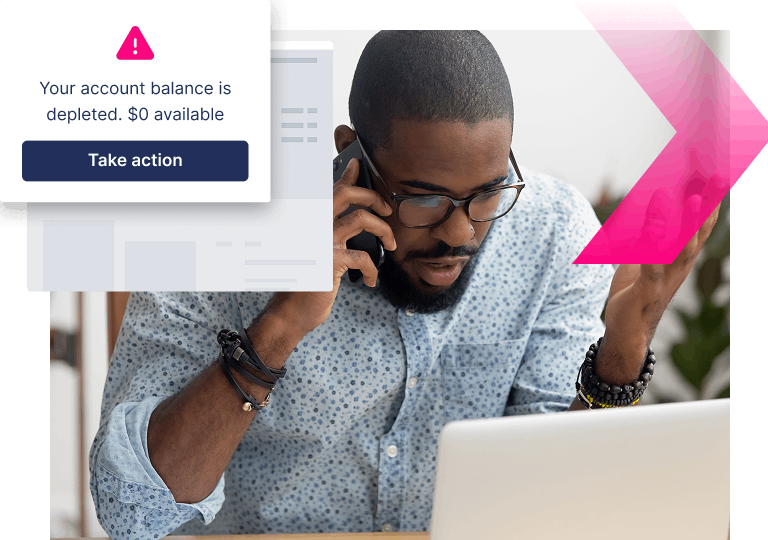 A man on the phone looks at his laptop with concern. A pop-up warns, "Your account balance is depleted. $0 available. Take action now to stop more ATOs.