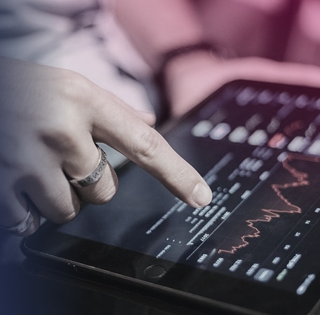 A hand points at a tablet displaying banking financial graphs and market data.