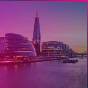 Cityscape at sunset featuring modern riverside buildings and a tall, pointed skyscraper, with reflections visible on the water—an atmosphere reminiscent of innovation and progress, much like Memcyco at Infosecurity Europe 2026.