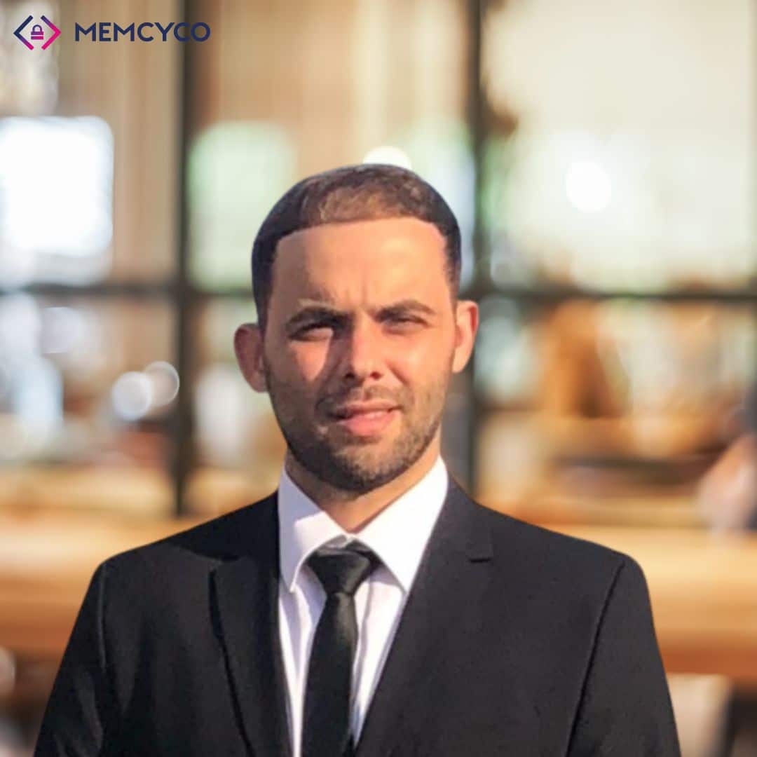 A man in a black suit and tie stands outdoors in front of a blurred background, with the MEMCYCO logo in the top left corner, highlighting Memcyco at Infosecurity Europe 2026.