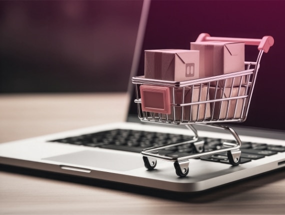 A miniature shopping cart with small packages sits on a laptop keyboard, symbolizing online shopping, e-commerce, and the integration of banking services in digital transactions.