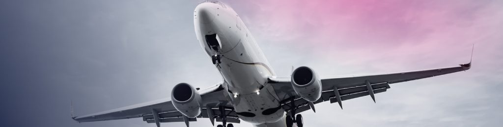 A commercial airplane is pictured from below as it flies against a cloudy sky with a pink and blue gradient, reminiscent of the innovative spirit driving the ecommerce and retail industries to new heights.